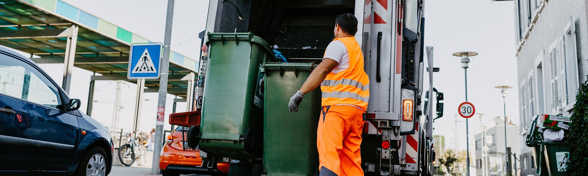 Ein Müllwerker bringt grüne Tonnen zum Müllwagen